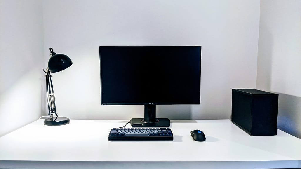 SFF PC FormD T1 on clean white desk with black lamp, keyboard, mouse and monitor
