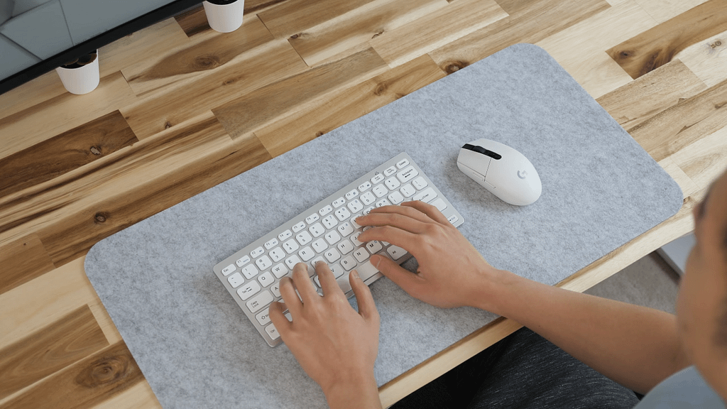 White Logitech G305 next to a white and silver small form factor keyboard on a grey mat